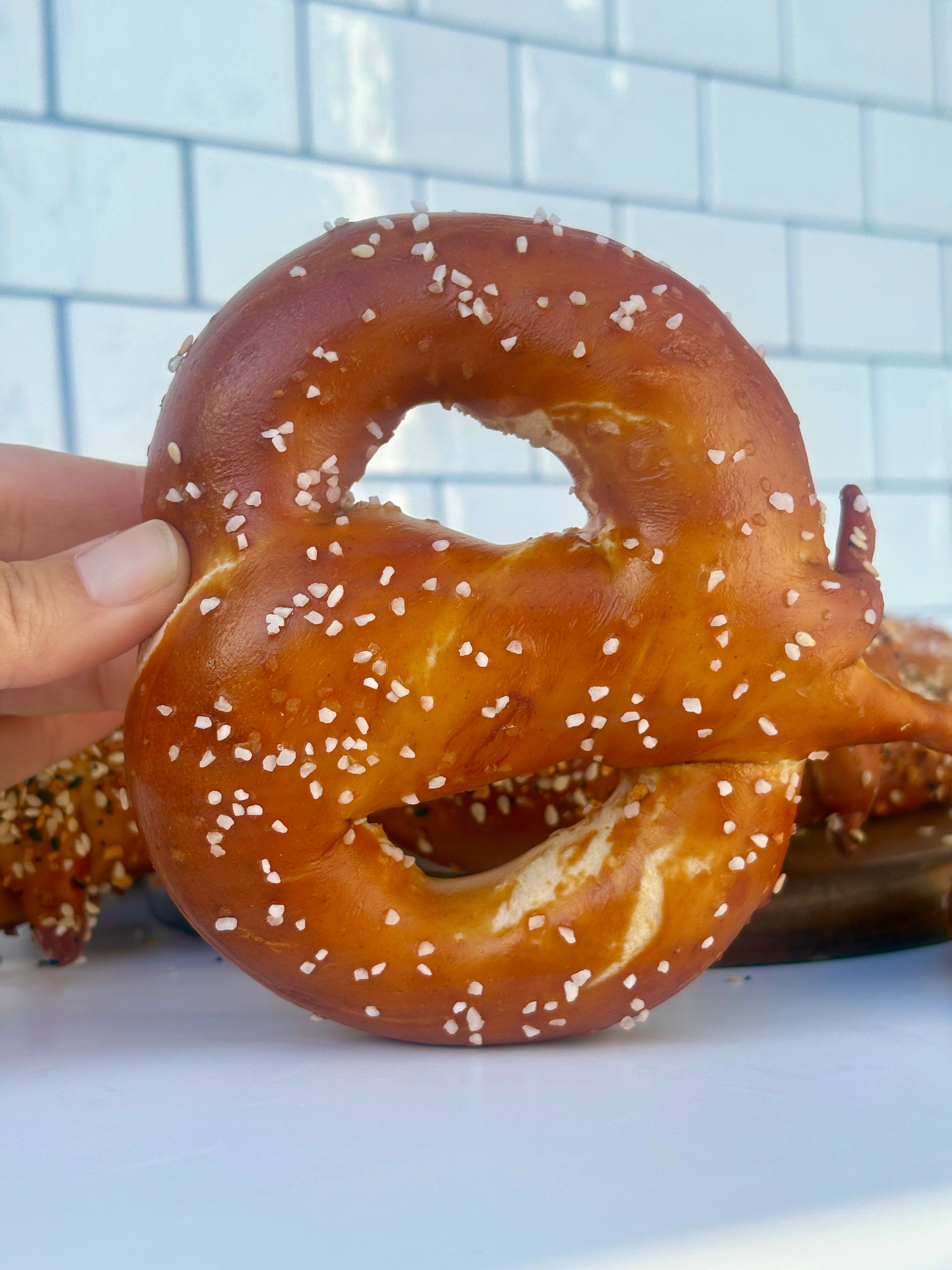 Hand holding a pretzel against a tiled wall background