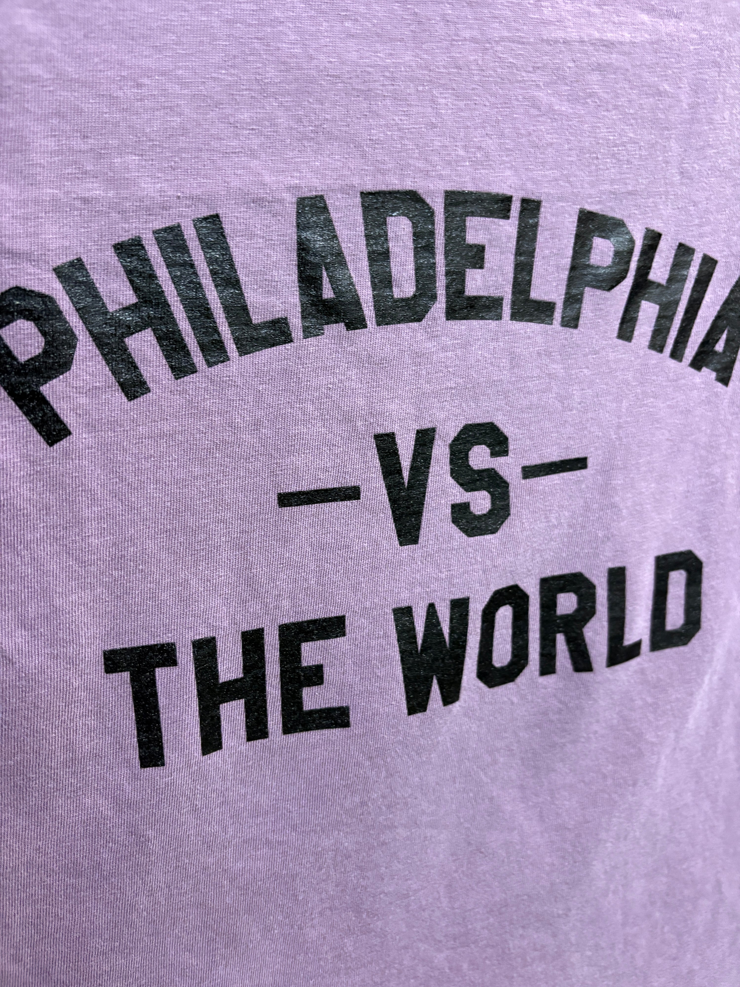 Close-up of a light lavender heather t-shirt with black distressed text reading 'PHILADELPHIA -VS- THE WORLD'.