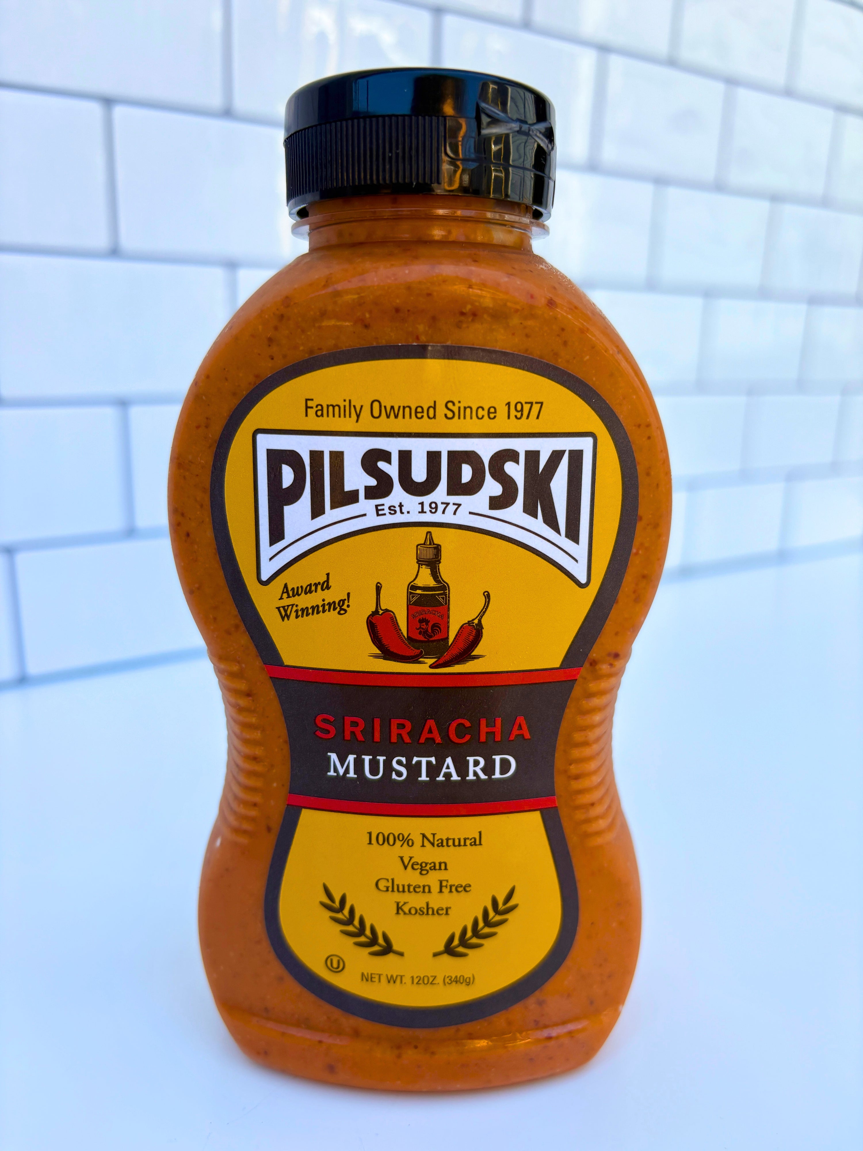 Bottle of Pilsudski Sriracha Mustard on a tiled wall background