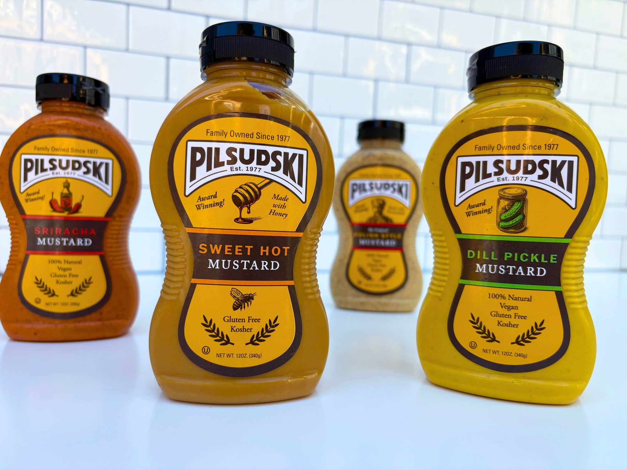 Four bottles of Pilsudski mustard on a white surface with a tiled wall background.